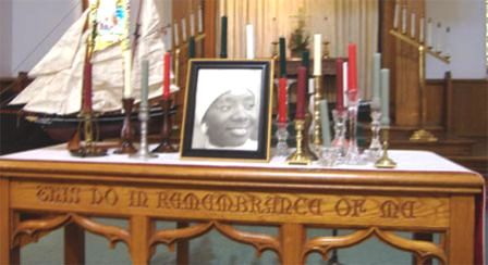 Photo of Kula Samba sits astride a table engraved with the Biblical words THIS DO IN REMEMBRANCE OF ME